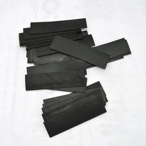 May include: A stack of black leather strips, likely for crafting or leatherworking projects.