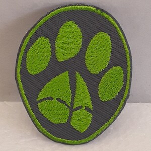 Peut inclure: Un écusson brodé gris et vert avec un motif de patte.