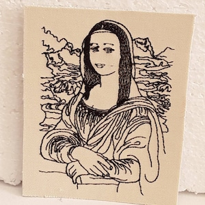 Può includere: Una toppa ricamata in bianco e nero che rappresenta la Gioconda, un famoso dipinto di Leonardo da Vinci. La toppa raffigura una donna con un sorriso gentile, vestita con un abito scuro e un foulard. Lo sfondo è un semplice paesaggio con montagne e acqua.