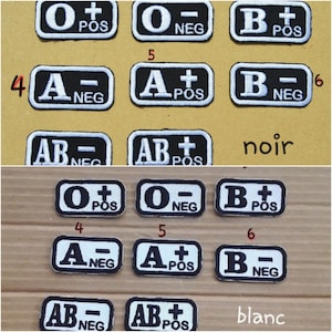Peut inclure: Un ensemble de 12 patchs de groupe sanguin, chacun avec un groupe sanguin différent, y compris O+, O-, A+, A-, B+, B-, AB+ et AB-. Les patchs sont blancs avec des lettres noires et sont disposés en deux rangées de six. Les patchs sont étiquetés "noir" et "blanc" en bas.