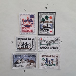 Peut inclure: Six écussons brodés ressemblant à des timbres-poste. Les écussons présentent divers motifs, dont une gondole, des palmiers, des personnages dans un bateau, des zèbres, des pyramides et des personnages avec un drapeau. Chaque écusson contient du texte indiquant le lieu ou le thème.