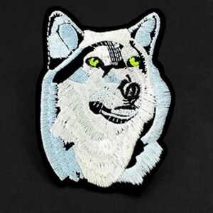 Op de afbeelding: Witte geborduurde wolfskop patch met groene ogen. De patch is op een zwarte achtergrond.
