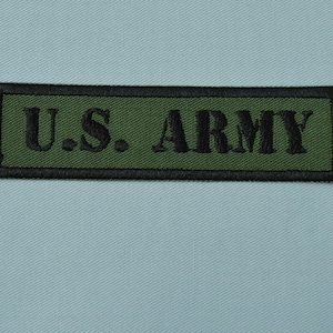 Può includere: Una toppa rettangolare verde con cuciture nere e il testo "U.S. ARMY" in nero.