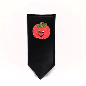 Pode incluir: Um marcador de página de couro preto com um design de abóbora sorridente vermelho e verde.