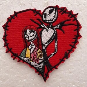 Puede incluir: Parche bordado con Jack Skellington y Sally de Pesadilla antes de Navidad. Están de pie dentro de un corazón rojo con costuras negras alrededor de los bordes.