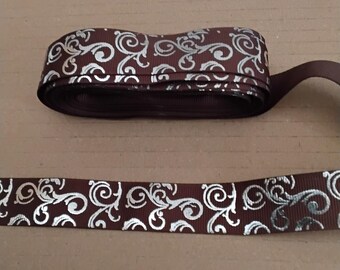May include: A roll of brown ribbon with a silver scroll pattern. The ribbon is folded over itself, with a length of ribbon extending from the roll. The ribbon is suitable for crafts, gift wrapping, and other decorative uses.