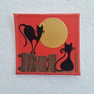 Peut inclure: Un patch brodé avec deux chats noirs en silhouette sur un fond rouge. Les chats sont assis sur une clôture brune avec un grand soleil doré derrière eux.