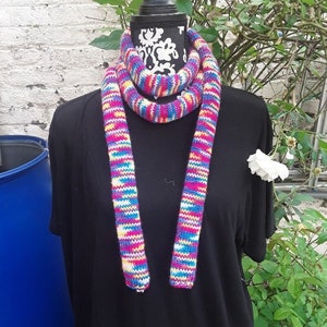 May include: A colorful striped knit scarf in shades of pink, blue, yellow, and white. The scarf is displayed on a black mannequin.