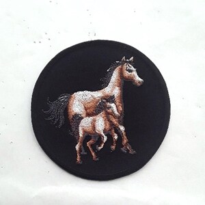 Peut inclure: Patch brodé représentant un cheval brun et blanc avec deux poulains. Le patch est circulaire et a un fond noir.