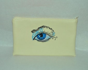May include: A white zippered pouch with a blue eye embroidered on the front. The eye has black eyelashes and a blue and white swirl design.