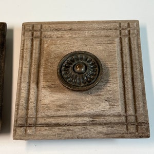 Peut inclure: Une porte de placard carrée en bois avec une poignée décorative. La porte est peinte en gris clair avec une texture en bois. La poignée est en métal et a un design circulaire.