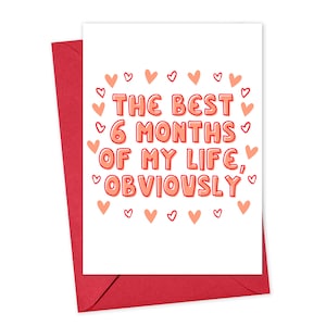 May include: A white card with a red envelope. The card has a pink and red heart border and the text 'THE BEST 6 MONTHS OF MY LIFE, OBVIOUSLY'.