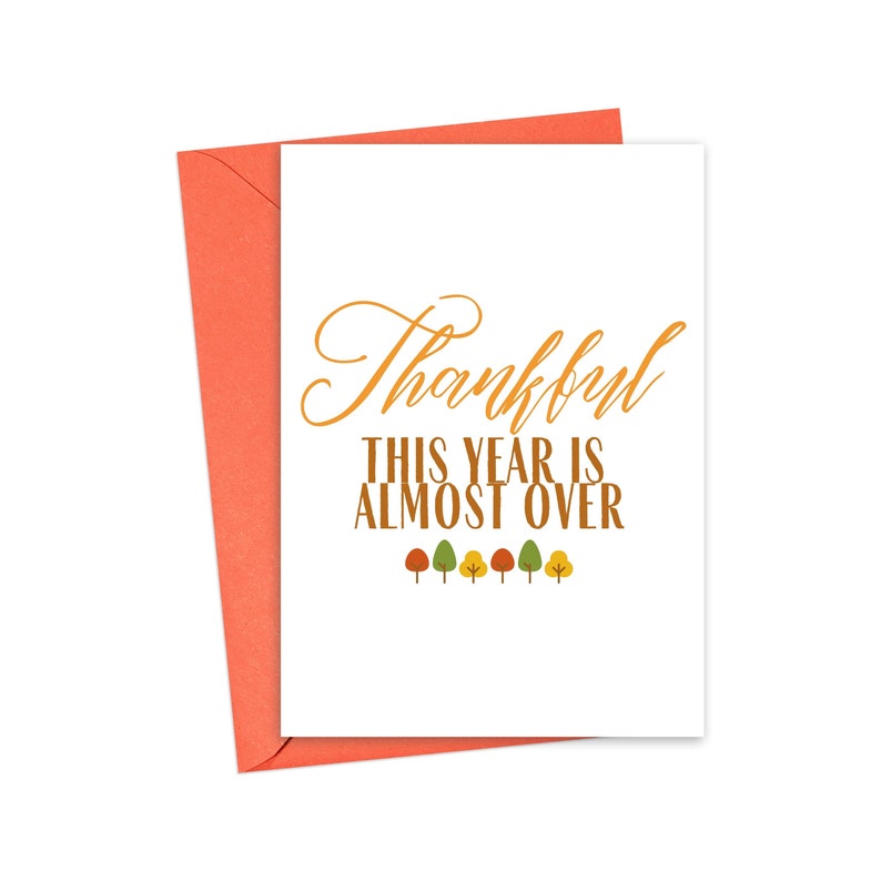 May include: A white card with a red envelope. The card has a gold cursive font that says "Thankful" and the text "This year is almost over" in brown font. There are six small stylized trees with orange, yellow, and green leaves.