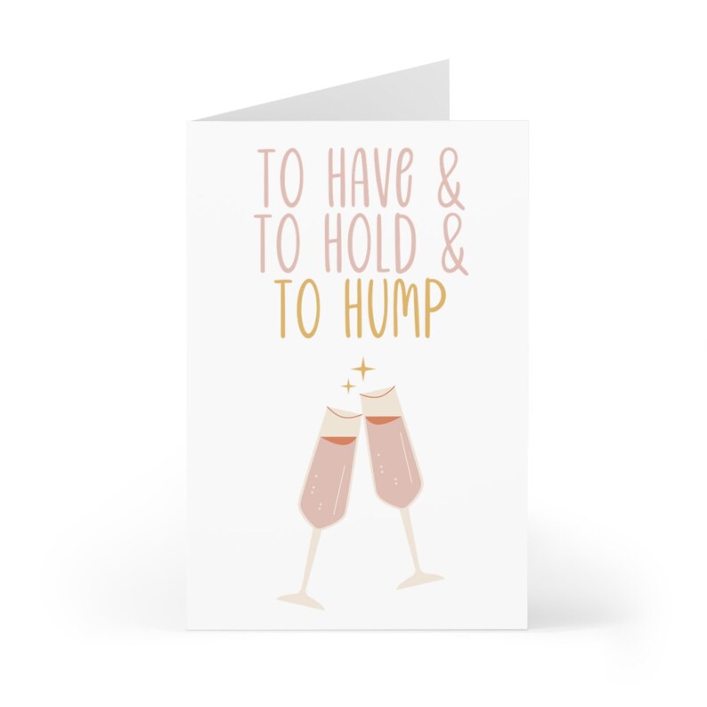 May include: A white card with the text "To have & to hold & to hump" in pink and gold lettering. Two pink champagne glasses clink together above the text.