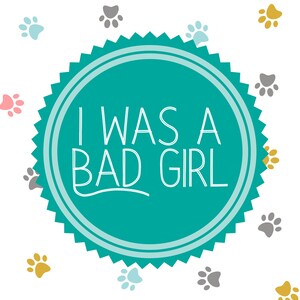 May include: A teal blue circle with a white border and a white starburst design around the edge. The circle has the text "I WAS A BAD GIRL" in white. The background is white with a pattern of grey, pink, and gold paw prints.