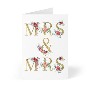 May include: Gold "Mrs. & Mrs." wedding card with floral accents in shades of pink, red, and green.