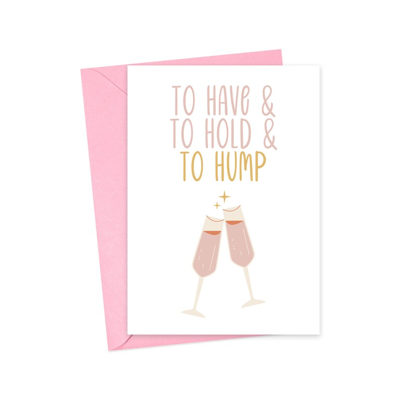 May include: A white card with pink trim and the text "To have & to hold & to hump" in gold lettering. Two pink champagne glasses clink together above the text.