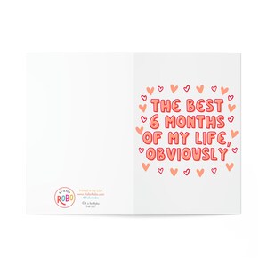 May include: A pink and white greeting card with the text "The best 6 months of my life, obviously" surrounded by pink hearts.