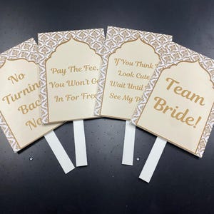 May include: Four decorative signs with white and gold patterns and text. The signs read: "No Turning Back, No", "Pay The Fee, You Won't Get In For Free", "If You Think Look Cute, Wait Until See My P", and "Team Bride!"