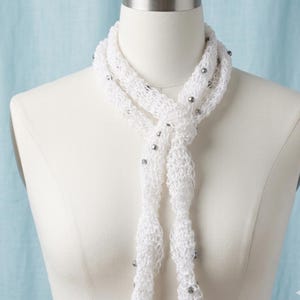May include: A white, open-weave scarf with silver beads. The scarf is displayed on a mannequin, showing its delicate texture and design. The scarf's ends hang down, highlighting the length and style.