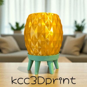 May include: A yellow pineapple-shaped decorative planter with a geometric pattern, sitting on a light teal base with three legs. The planter is on a wooden table. The text "kcc3Dprint" is at the bottom.