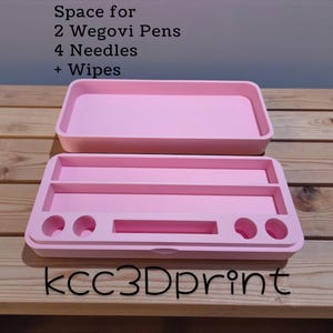 Puede incluir: Un organizador rosa claro de dos piezas con el texto "Space for 2 Wegovi Pens 4 Needles + Wipes" y "kcc3Dprint". La parte superior es una bandeja simple. La parte inferior tiene compartimentos para bolígrafos, agujas y toallitas. El organizador está sobre una superficie de madera.
