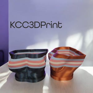 Pode incluir: Dois vasos de plantas impressos em 3D, um em azul escuro e outro em cobre, ambos com um design de listras horizontais em rosa, branco e azul.