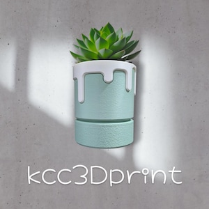 May include: A light blue and white decorative planter with a succulent plant. The planter has a unique design with a white dripping effect around the top. The text "kcc3Dprint" is at the bottom.