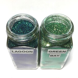 K&ouml;nnte beinhalten: Zwei Glasbeh&auml;lter gef&uuml;llt mit gr&uuml;nem Glitter. Der Beh&auml;lter links ist mit "LAGOON" beschriftet und der Beh&auml;lter rechts mit "GREEN BAY".