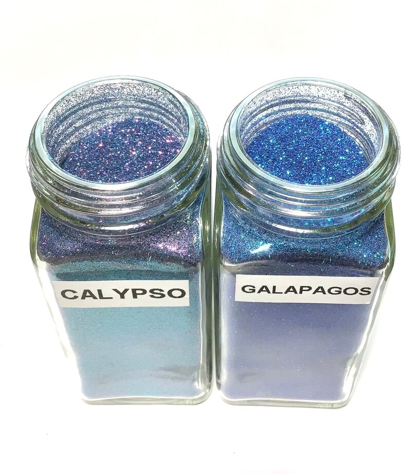 K&ouml;nnte beinhalten: Zwei Glasbeh&auml;lter gef&uuml;llt mit blauem Glitter. Der Beh&auml;lter links ist mit "CALYPSO" beschriftet und der Beh&auml;lter rechts mit "GALAPAGOS".