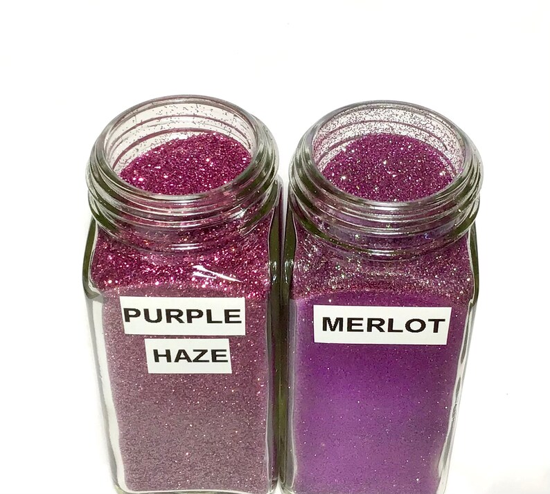K&ouml;nnte beinhalten: Zwei Glasbeh&auml;lter gef&uuml;llt mit lila Glitter. Der Beh&auml;lter links ist mit "Purple Haze" beschriftet und der Beh&auml;lter rechts mit "Merlot".