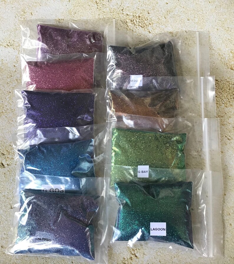 K&ouml;nnte beinhalten: Acht kleine Beutel mit schimmerndem Glitter, jeder mit einer anderen Farbe und einem anderen Namen. Die Farben sind Lila, Rosa, Blau, T&uuml;rkis, Gr&uuml;n und zwei Gr&uuml;nt&ouml;ne. Die Namen sind "Midnight", "Rose Gold", "Amethyst", "Lagoon", "Sea Glass", "Green Bay" und "Calpyso".