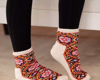May include: A pair of patterned socks with a white foot and cuff, and a colorful design of red, orange, blue, and yellow. The socks are worn with black leggings. The socks are made of a soft, warm material.