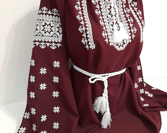 May include: A maroon embroidered blouse with white floral patterns and a white braided belt with tassels.
