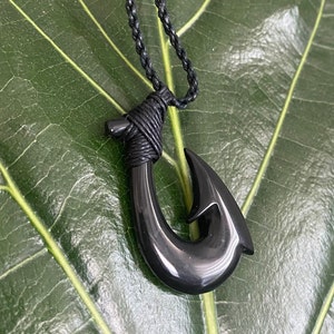 May include: Black hook necklace with a black cord. The hook is made of polished black material and is shaped like a traditional Hawaiian fish hook.