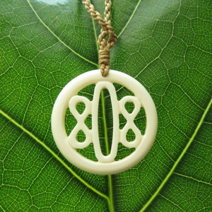 May include: A white bone pendant necklace with a carved design of a stylized butterfly. The necklace is on a green leaf background.