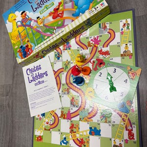 以下が含まれることがあります： セサミストリートのChutes and Laddersボードゲーム。ゲーム盤、箱、説明書、ゲームの駒が含まれています。箱にはビッグバード、エルモ、クッキーモンスターが描かれています。ゲーム盤にははしごや滑り台があります。