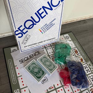 May include: A Sequence board game set. The box is white with the word "SEQUENCE" in large blue letters. The game includes a game board, two decks of cards, and colored game chips in green, red, and blue.