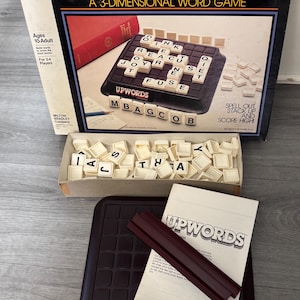 May include: A vintage board game called Upwords, a 3-dimensional word game. The box is brown with red and yellow lettering. The game board is black with white letter tiles. The game includes a set of letter tiles and a score pad.
