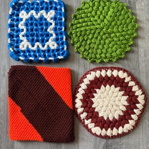 May include: Four colorful, handmade crochet items are displayed. A blue and white square, a green circular piece, a square with orange and brown diagonal stripes, and a maroon and cream circular piece.