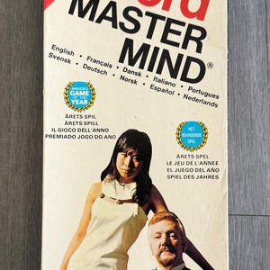 May include: A vintage Word Master Mind game box. The box features the game title in large red and black letters. The box also includes the text "New Improved Version" and "Game of the Year". The box art shows a woman and a man.