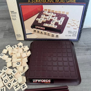 May include: A vintage board game called Upwords, a 3-dimensional word game. The game includes a brown game board with a grid of squares, white letter tiles, and a box with instructions. The box has a picture of the game board with letters already placed on it, and the words "MBAGCOB" and "FUSE" are visible.