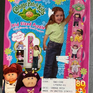 May include: A Cabbage Patch Kids Kid Sized Puzzle box with a growth chart feature. The box is pink and blue with images of Cabbage Patch Kids dolls and a young girl. Includes 10 height stickers and glue.