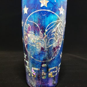 Op de afbeelding: Een blauwe en paarse galaxy-thema beker met een zilveren glitterafwerking. De beker heeft een zilveren omtrek van twee handen die in elkaar grijpen in de vorm van een hart, omringd door zilveren sterren. Het woord "Friends" staat in zilveren glitter op de bodem van de beker.