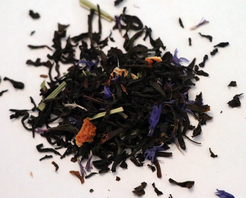 May include: A close-up of a blend of black tea leaves, dried orange peel, and blue cornflower petals.