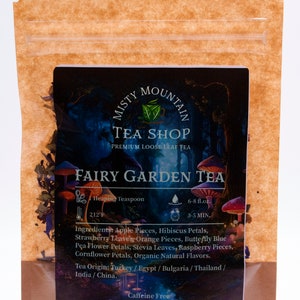 Op de afbeelding: Een bruine papieren zak met een hersluitbare ritssluiting. De voorkant van de zak heeft een kleurrijk etiket met de tekst "Misty Mountain Tea Shop Premium Loose Leaf Tea Fairy Garden Tea". Het etiket bevat ook een lijst met ingredi&euml;nten, instructies voor het zetten en de tekst "Cafe&iuml;nevrij".