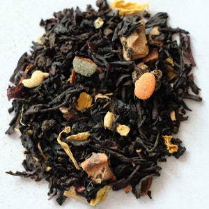 May include: A close-up of a blend of black tea leaves, dried fruit pieces, and spices. The tea blend is a mix of black tea, orange peel, cinnamon, and other spices.