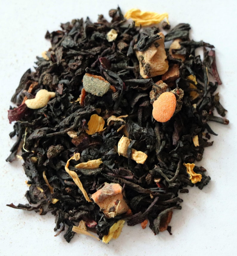 May include: A close-up of a blend of black tea leaves, dried fruit pieces, and spices. The tea blend is a mix of black tea, orange peel, cinnamon, and other spices.