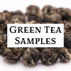 May include: Close-up of green tea samples, featuring tightly rolled tea leaves. The image has a white background with a rectangular sign that reads "GREEN TEA SAMPLES" in black text. The tea leaves are a mix of green and brown.