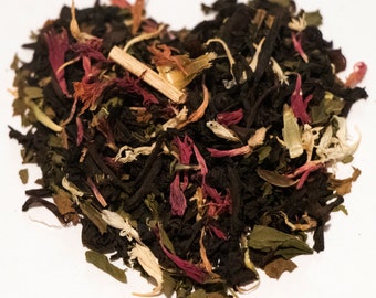 May include: A heart-shaped pile of loose leaf tea blend with black tea, green tea, dried fruit pieces, and flower petals.